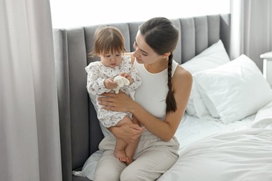 Beautiful young mother and her cute little baby with rabbit toy on bed at home