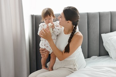 Beautiful young mother and her cute little baby with rabbit toy on bed at home