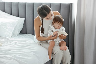 Beautiful young mother and her cute little baby with rabbit toy on bed at home