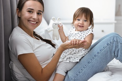 Beautiful young mother and her cute little baby with rabbit toy on bed at home