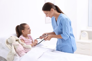 Doctor examining little girl on bed at hospital