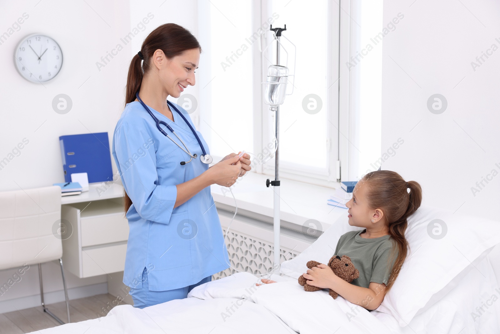 Photo of Doctor examining little girl and setting IV drip on bed at hospital