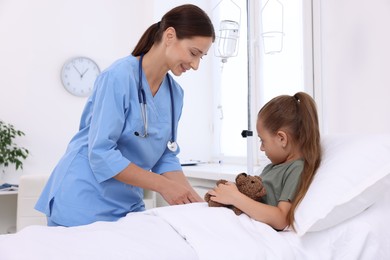 Photo of Doctor examining little girl and setting IV drip on bed at hospital