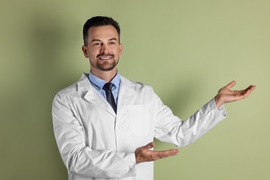 Smiling doctor pointing at something on olive background