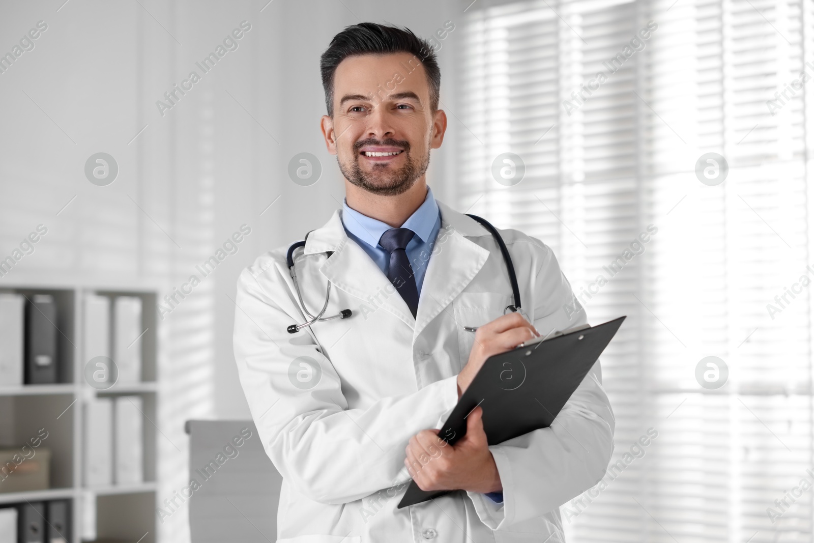 Photo of Smiling doctor with stethoscope and clipboard in clinic