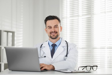 Smiling doctor working with laptop at table in clinic