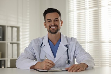 Photo of Smiling doctor with clipboard at table in clinic