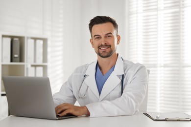 Smiling doctor working with laptop at table in clinic