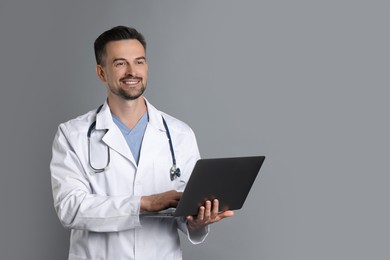 Photo of Smiling doctor with stethoscope and laptop on grey background