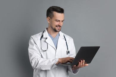 Smiling doctor with stethoscope and laptop on grey background