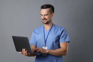 Photo of Smiling nurse with badge using laptop on grey background