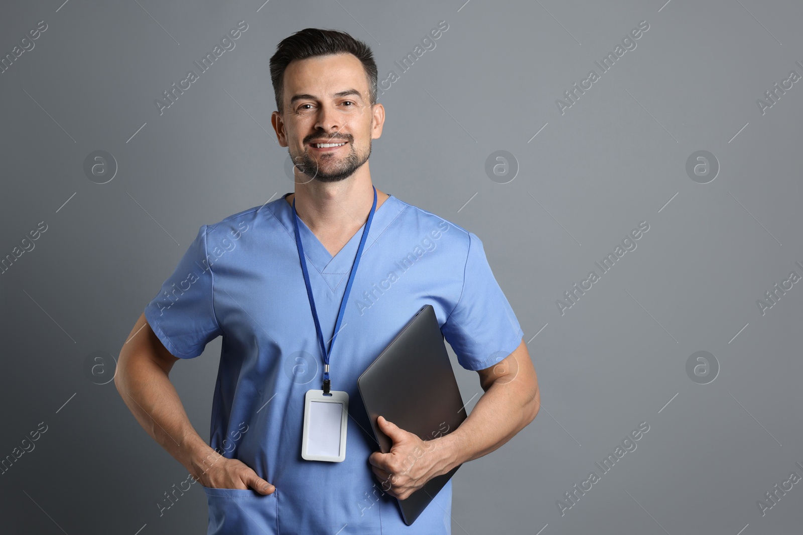 Photo of Smiling nurse with badge and laptop on grey background, space for text