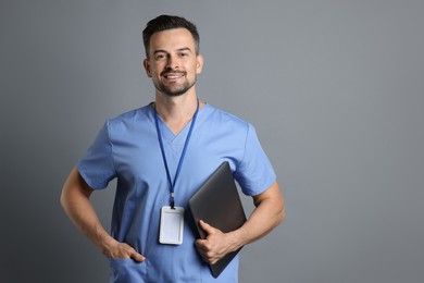 Photo of Smiling nurse with badge and laptop on grey background, space for text