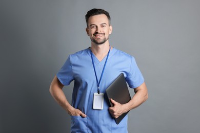 Smiling nurse with badge and laptop on grey background