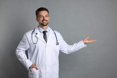 Photo of Smiling doctor with stethoscope pointing at something on grey background