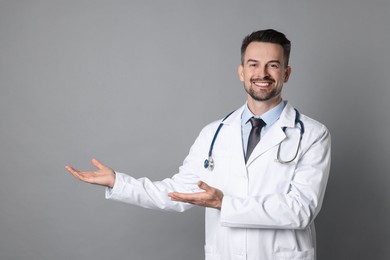 Photo of Smiling doctor with stethoscope pointing at something on grey background