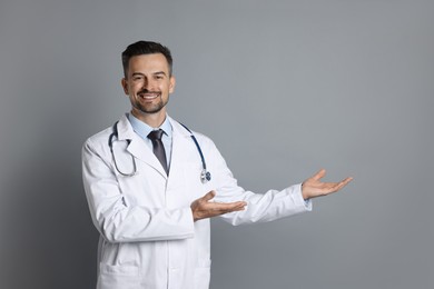 Photo of Smiling doctor with stethoscope pointing at something on grey background