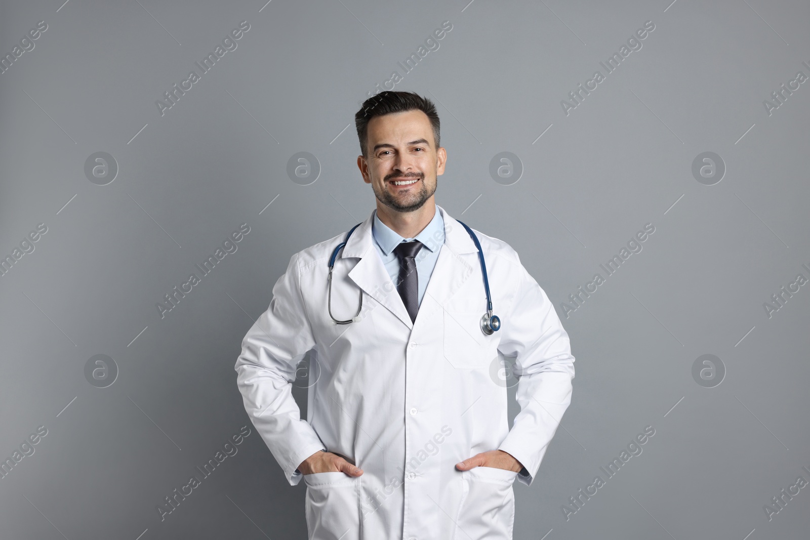 Photo of Smiling doctor with stethoscope on grey background