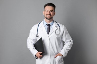 Photo of Smiling doctor with stethoscope and clipboard on grey background