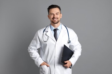 Photo of Smiling doctor with stethoscope and clipboard on grey background