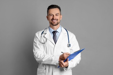 Photo of Smiling doctor with stethoscope and clipboard on grey background