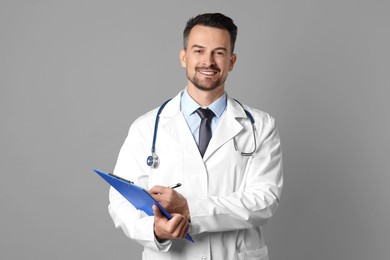 Photo of Smiling doctor with stethoscope and clipboard on grey background