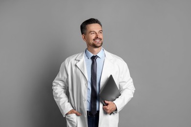 Smiling doctor with laptop on grey background