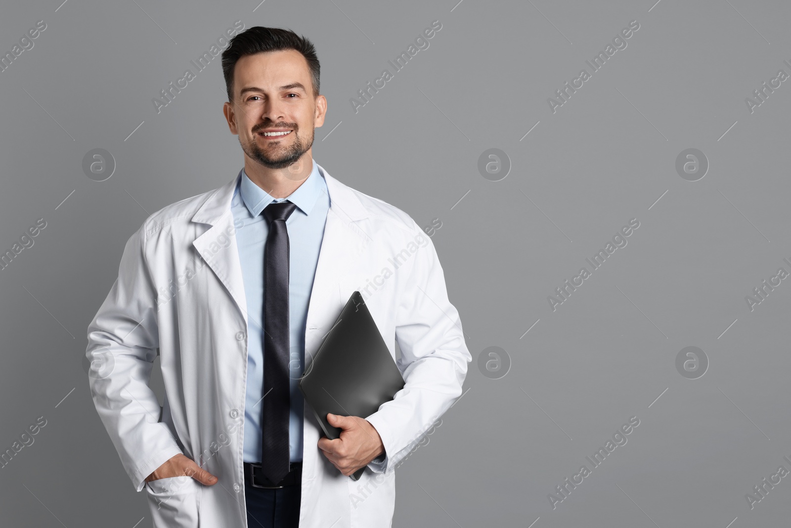 Photo of Smiling doctor with laptop on grey background, space for text