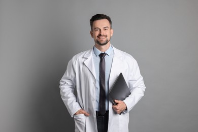 Smiling doctor with laptop on grey background