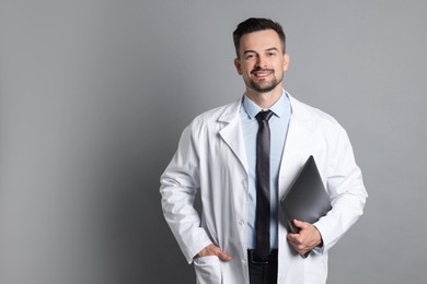 Smiling doctor with laptop on grey background