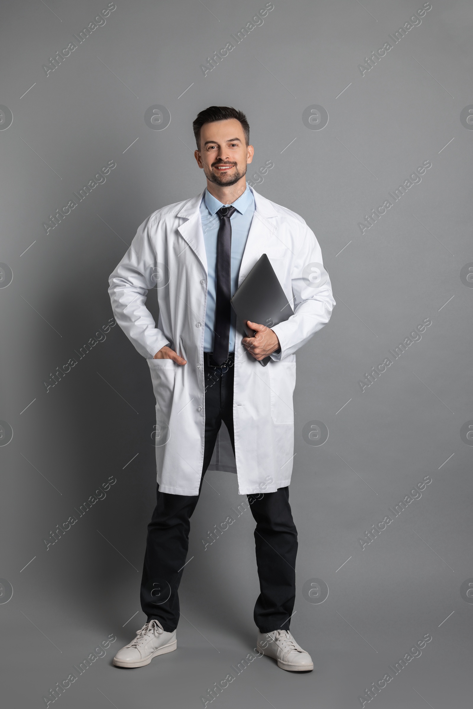 Photo of Smiling doctor with laptop on grey background