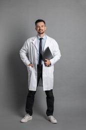 Smiling doctor with laptop on grey background