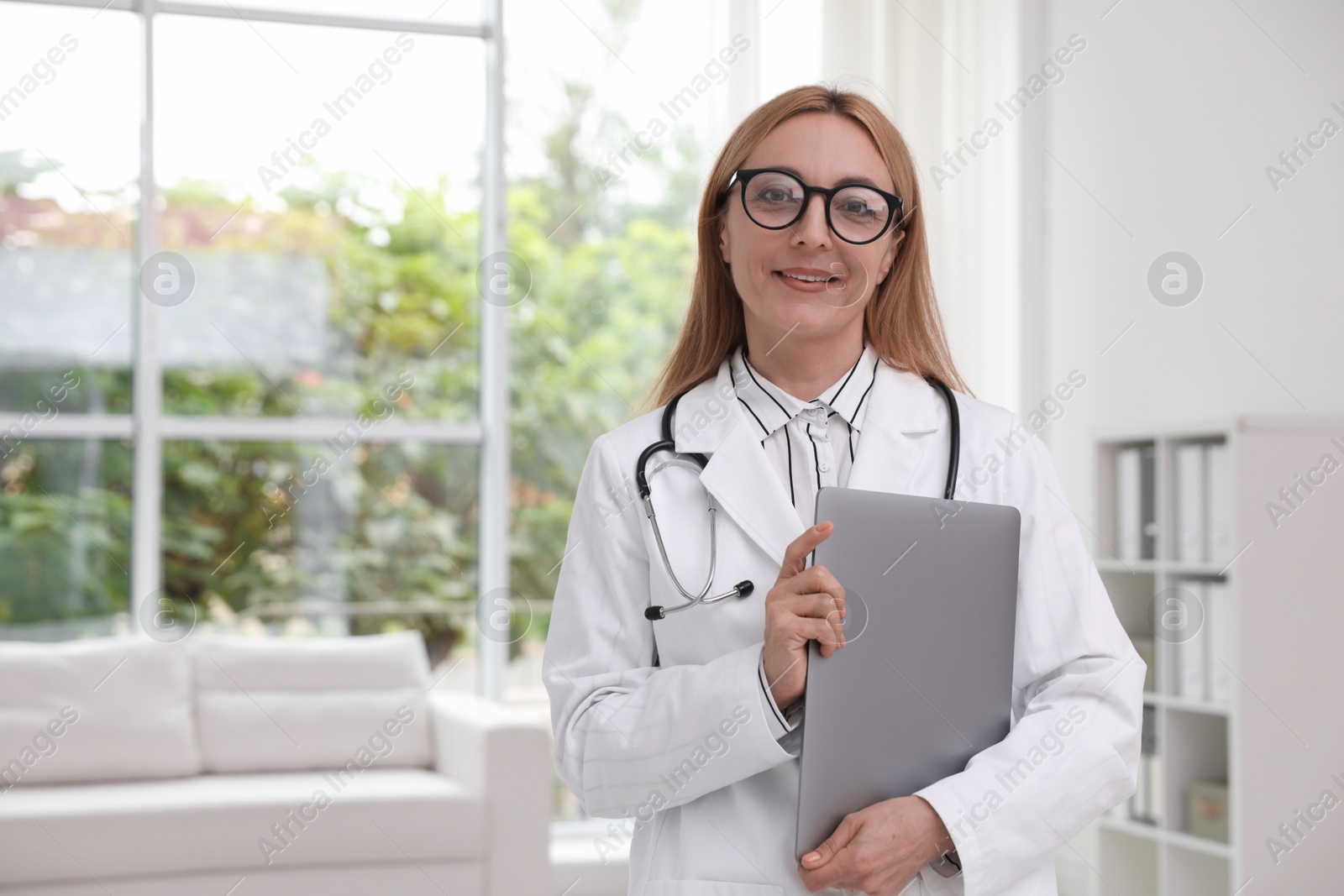 Photo of Smiling doctor with stethoscope and laptop in clinic