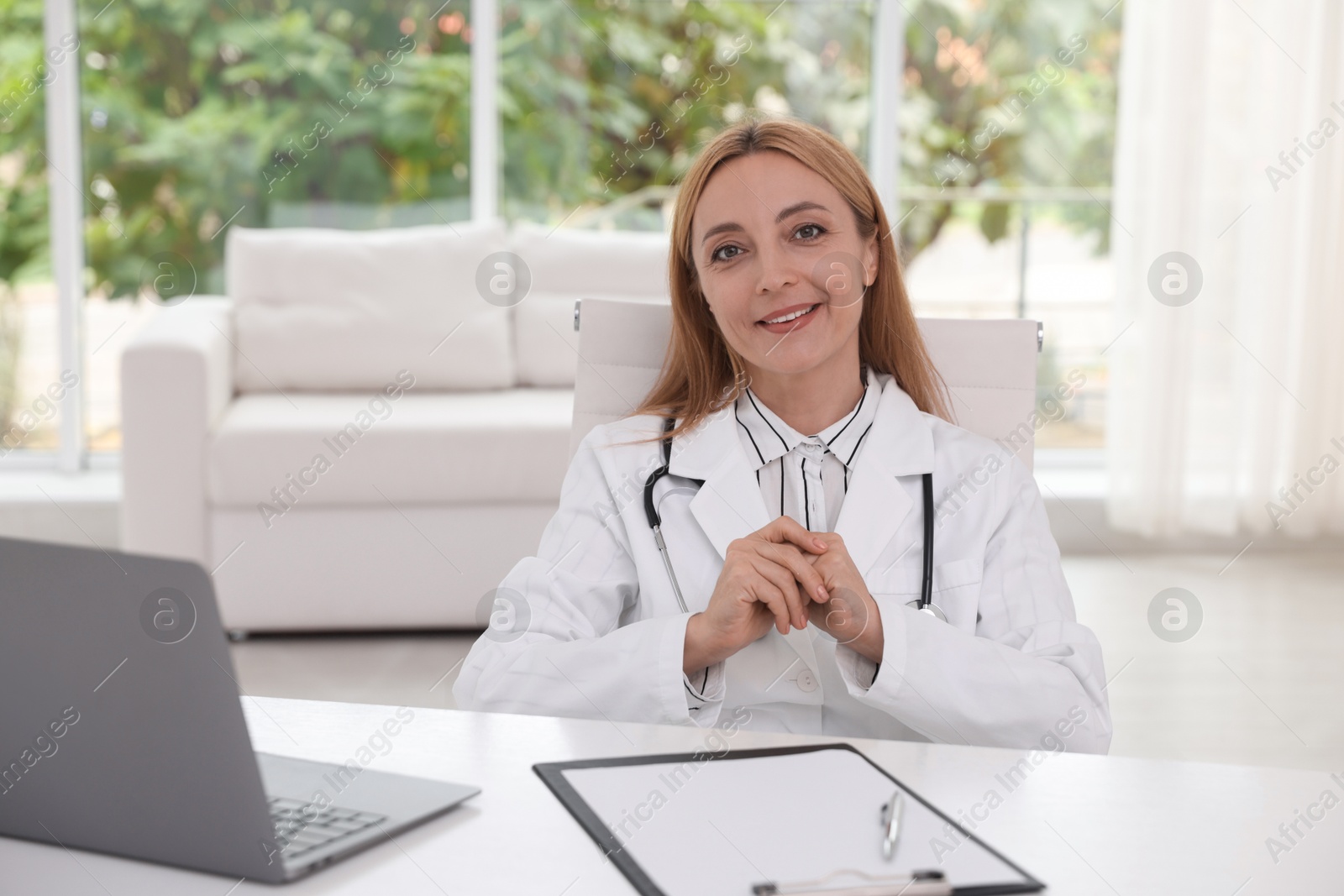 Photo of Doctor with stethoscope, laptop and clipboard at table in clinic