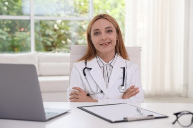 Doctor with stethoscope, laptop and clipboard at table in clinic