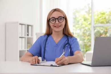 Doctor with stethoscope, laptop and clipboard at table in clinic