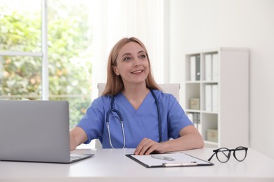 Doctor with stethoscope, laptop and clipboard at table in clinic