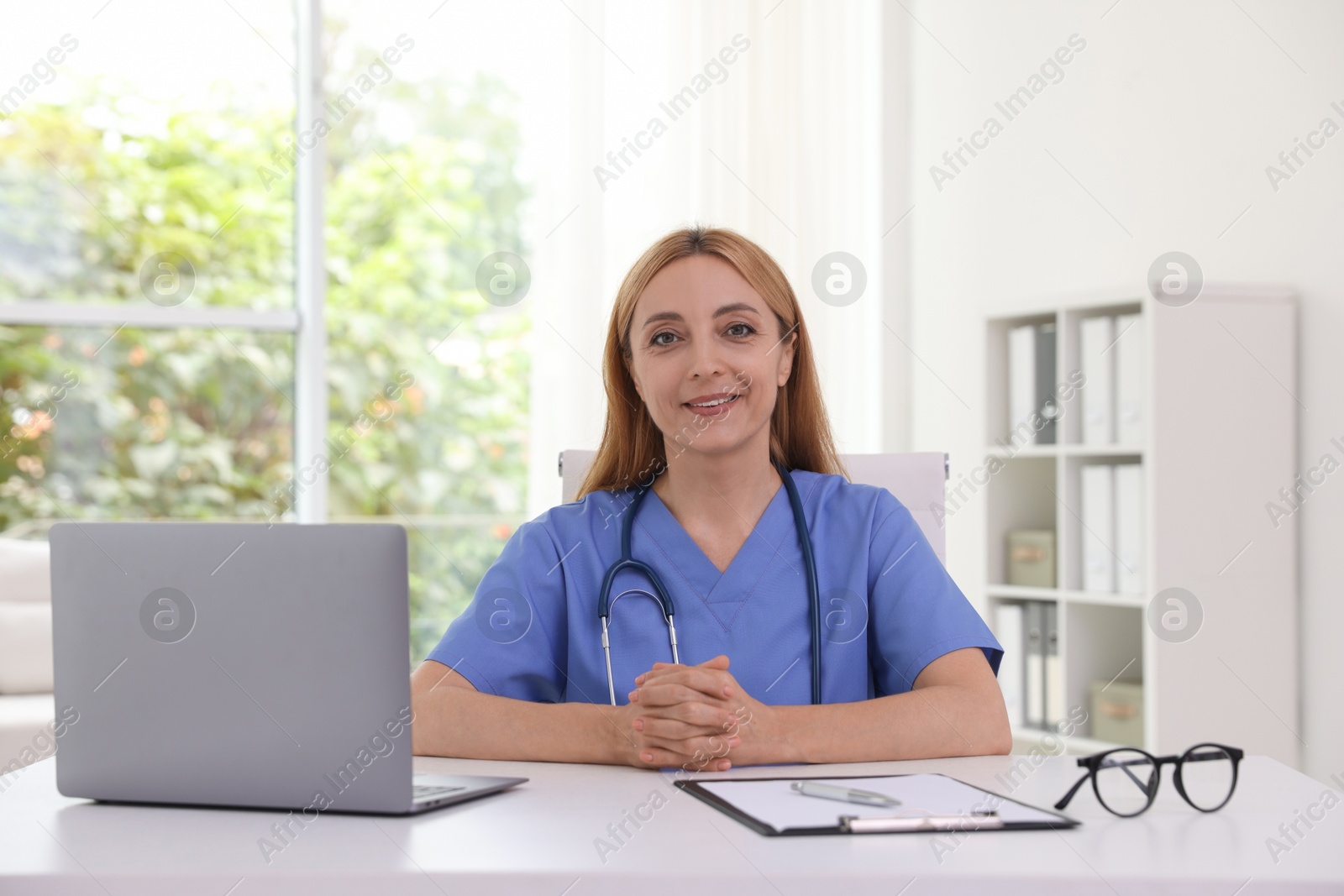 Photo of Doctor with stethoscope, laptop and clipboard at table in clinic