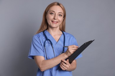 Doctor with clipboard writing notes on gray background