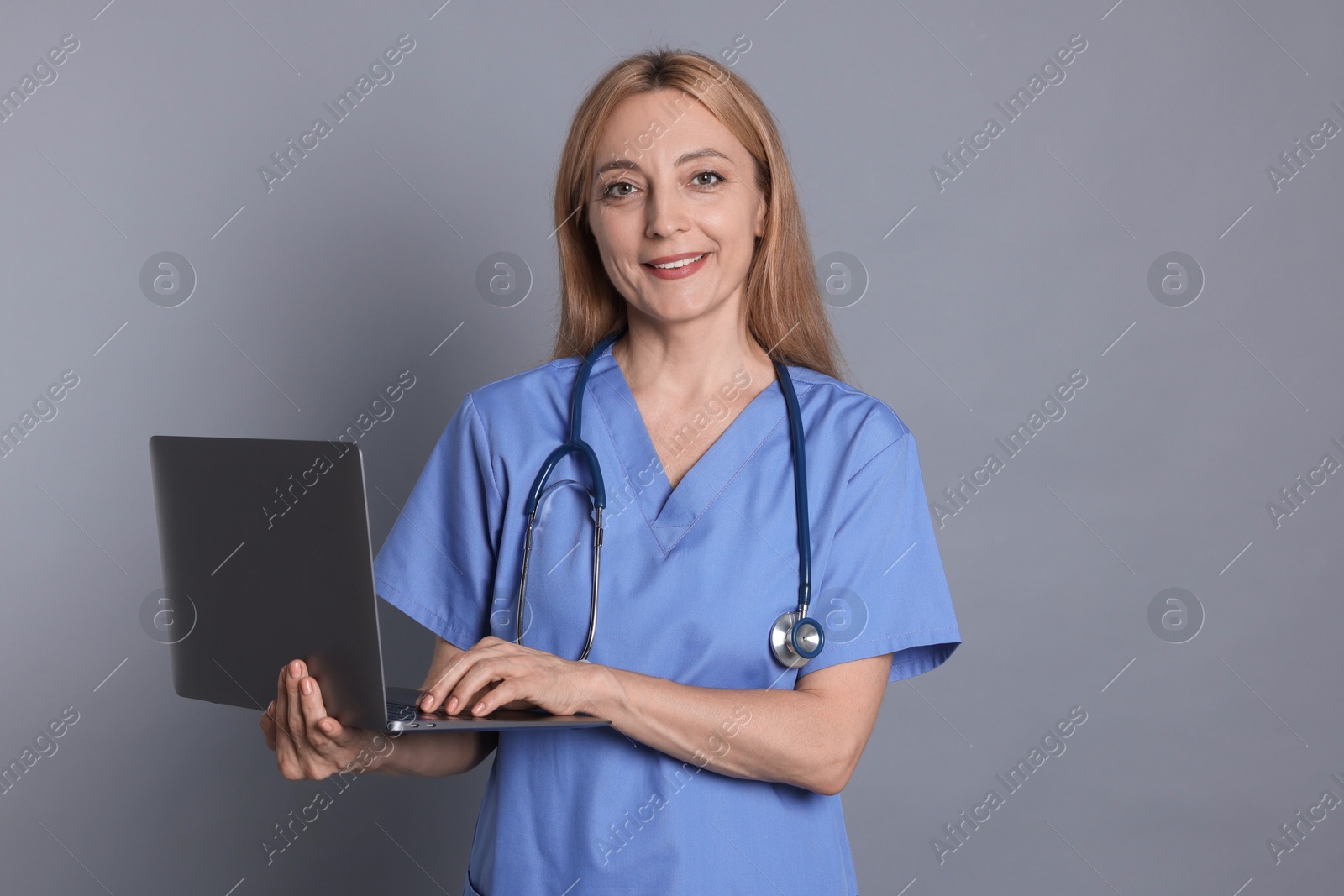 Photo of Doctor with stethoscope and laptop on gray background