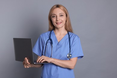 Doctor with stethoscope and laptop on gray background