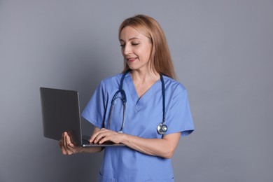 Doctor with stethoscope using laptop on gray background