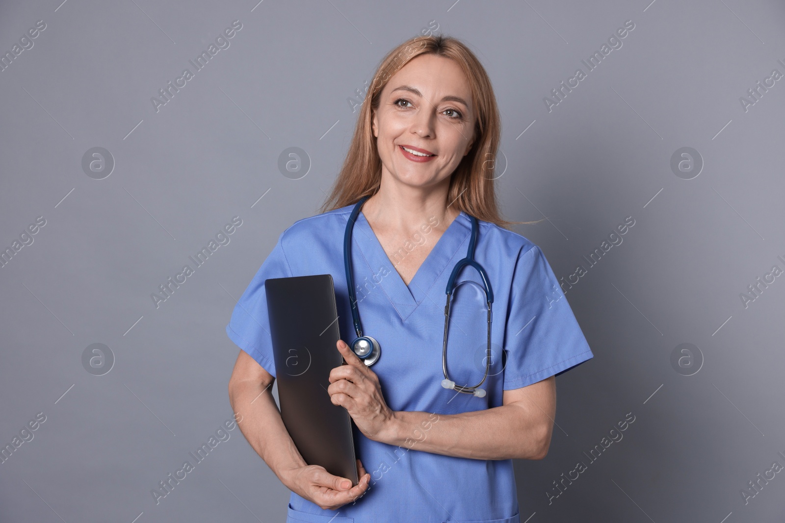 Photo of Doctor with stethoscope and laptop on gray background