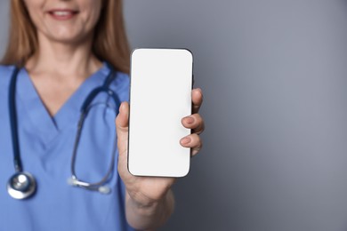 Doctor showing smartphone with blank screen on gray background, closeup. Mockup for design