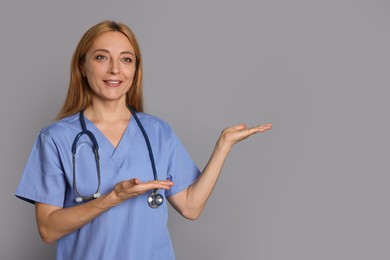 Doctor with stethoscope showing something on gray background, space for text