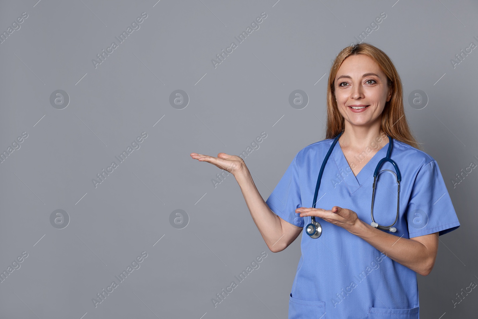 Photo of Doctor with stethoscope showing something on gray background, space for text