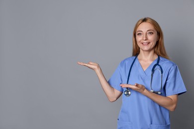 Doctor with stethoscope showing something on gray background, space for text