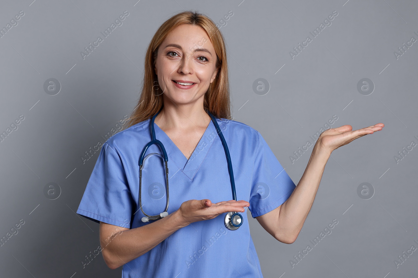 Photo of Doctor with stethoscope showing something on gray background