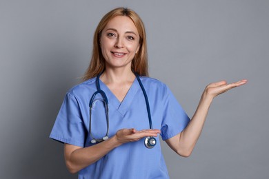 Doctor with stethoscope showing something on gray background