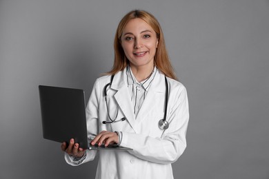 Photo of Doctor with stethoscope and laptop on gray background